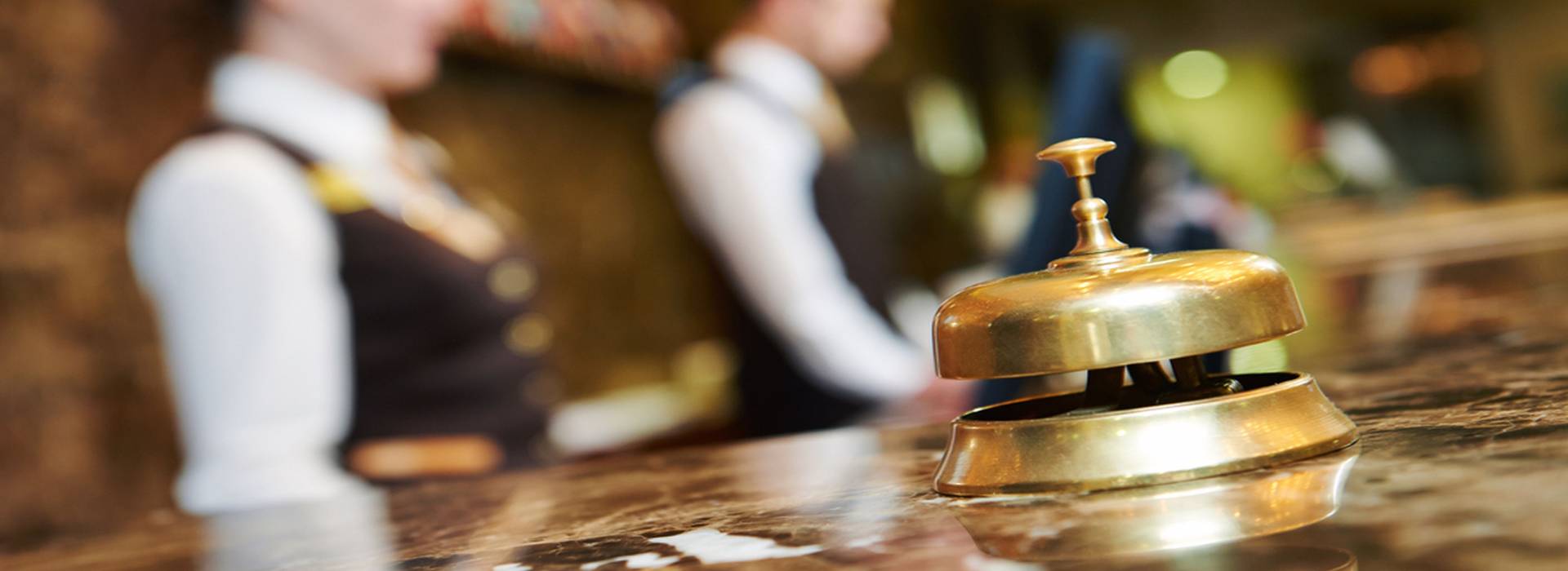 A hotel receptionist and concierge in tailored navy hospitality vests standing at a wood-paneled front desk